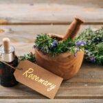 Rosemary essential oil and fresh blooming twig in a wooden mortar, wooden table, tag with text rosemary